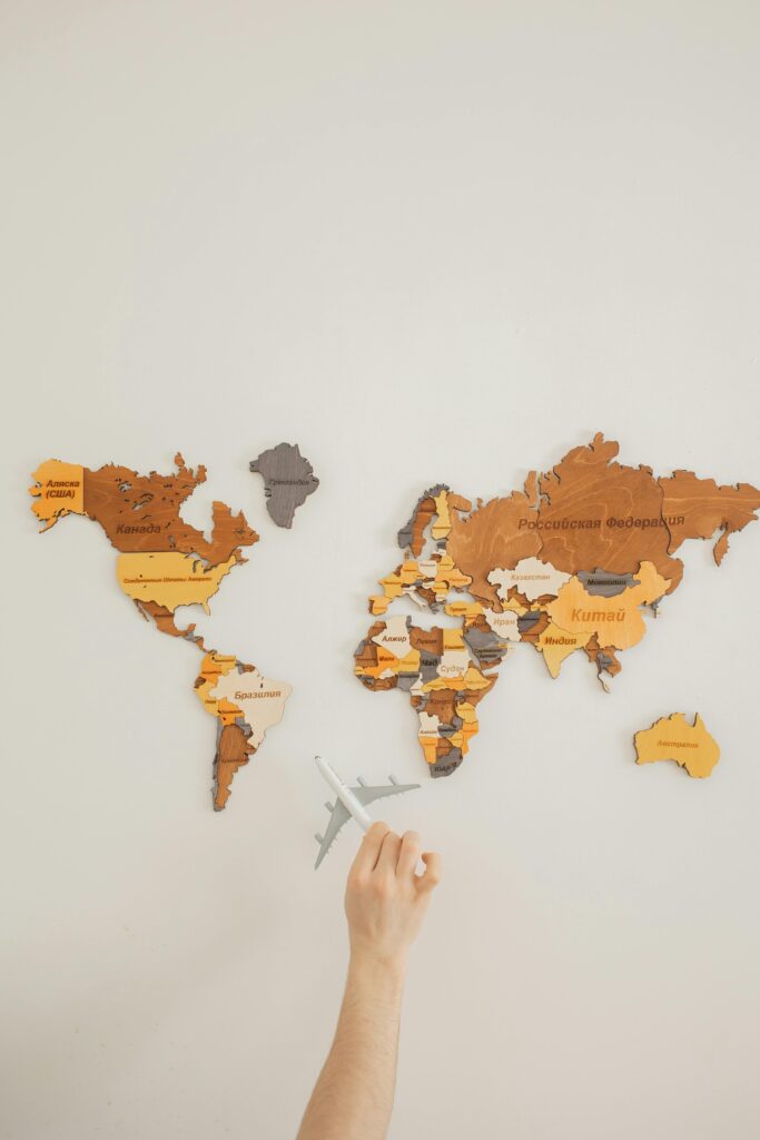 pexels photo 7412104 7412104 A hand holding a toy plane points to a colorful decorative world map on a wall.